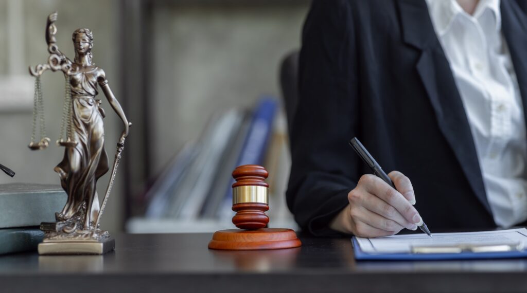 Statue of Justice and female lawyer in suit at workplace with laptop, gavel and femida in office.